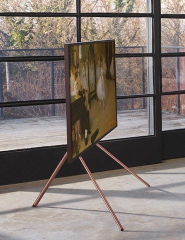 거실에 TV와 스튜디오 스탠드가 결합된 제품이 측면으로 놓여있고, 화면에는 명화 그림이 보입니다.