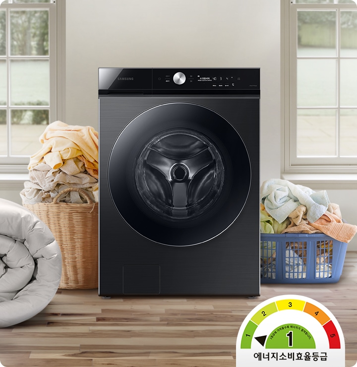 정면 가운데에 그랑데AI 세탁기 정면샷이 보입니다. 세탁기의 왼편에는 대형이불이있고 좌우로 많은 빨래가 보입니다. 화면 오른쪽 끝에는 바구리를 머리에 쓰고 웃고 있는 아이의 모습이 보입니다. 왼편 상단 위에는 에너지 소비효율 1등급 표시가 되어 있습니다.