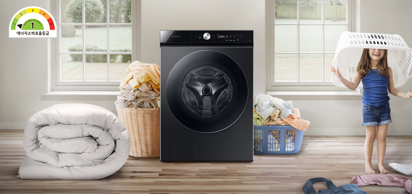 정면 가운데에 그랑데AI 세탁기 정면샷이 보입니다. 세탁기의 왼편에는 대형이불이있고 좌우로 많은 빨래가 보입니다. 화면 오른쪽 끝에는 바구리를 머리에 쓰고 웃고 있는 아이의 모습이 보입니다. 왼편 상단 위에는 에너지 소비효율 1등급 표시가 되어 있습니다.