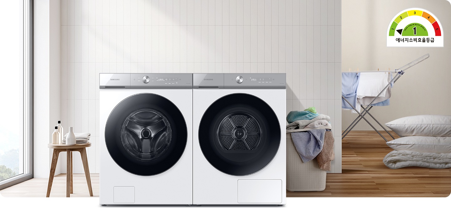 화이트톤의 욕실에 그랑데AI 세탁기와 건조기가 병렬로 배치되어 있고 우측에는 빨래건조대와, 많은양의 빨래, 이불이 배치되어 있으며, 좌측에는 세제가 놓여진 미니테이블이 있습니다.