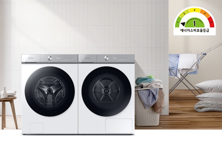 화이트톤의 욕실에 그랑데AI 세탁기와 건조기가 병렬로 배치되어 있고 우측에는 빨래건조대와, 많은양의 빨래, 이불이 배치되어 있으며, 좌측에는 세제가 놓여진 미니테이블이 있습니다.