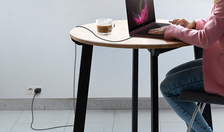 테이블 위에 커피와 노트북이 놓여져있고, 그 앞에 의자에 앉아있는 여성이 노트북을 하고 있습니다. 노트북에는 C to C 케이블이 꽂혀져 있습니다. 케이블이 길다는것을 알려주는 이미지 입니다.
