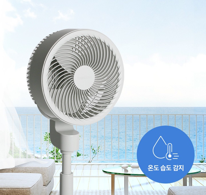 푸른 바다가 보이는 테라스에 선풍기가 놓여져 있습니다. 온도 습도 감지 아이콘이 보입니다.