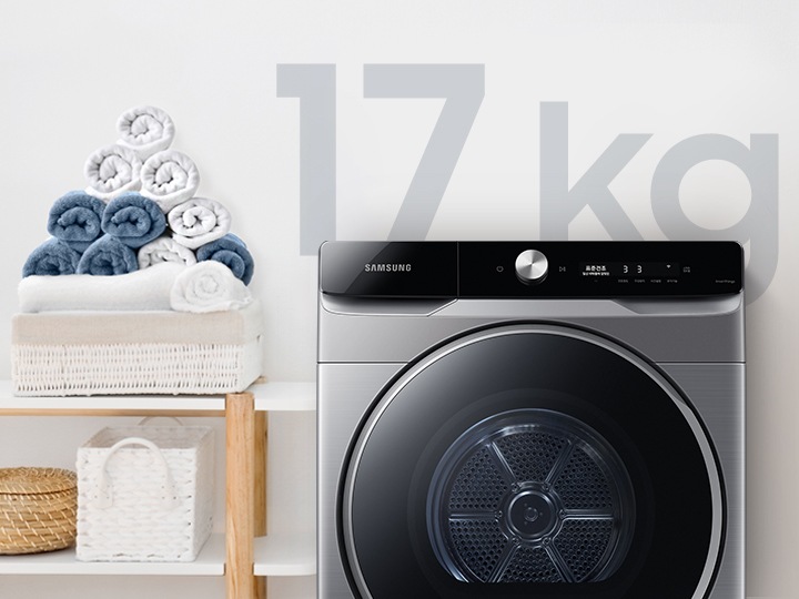 욕실로 보이는 공간에 삼성 그랑데 건조기 AI 제품이 놓여져 있습니다. 왼쪽 선반에는 수건이 쌓여져 있고 그 밑에는 바구니가 있습니다.