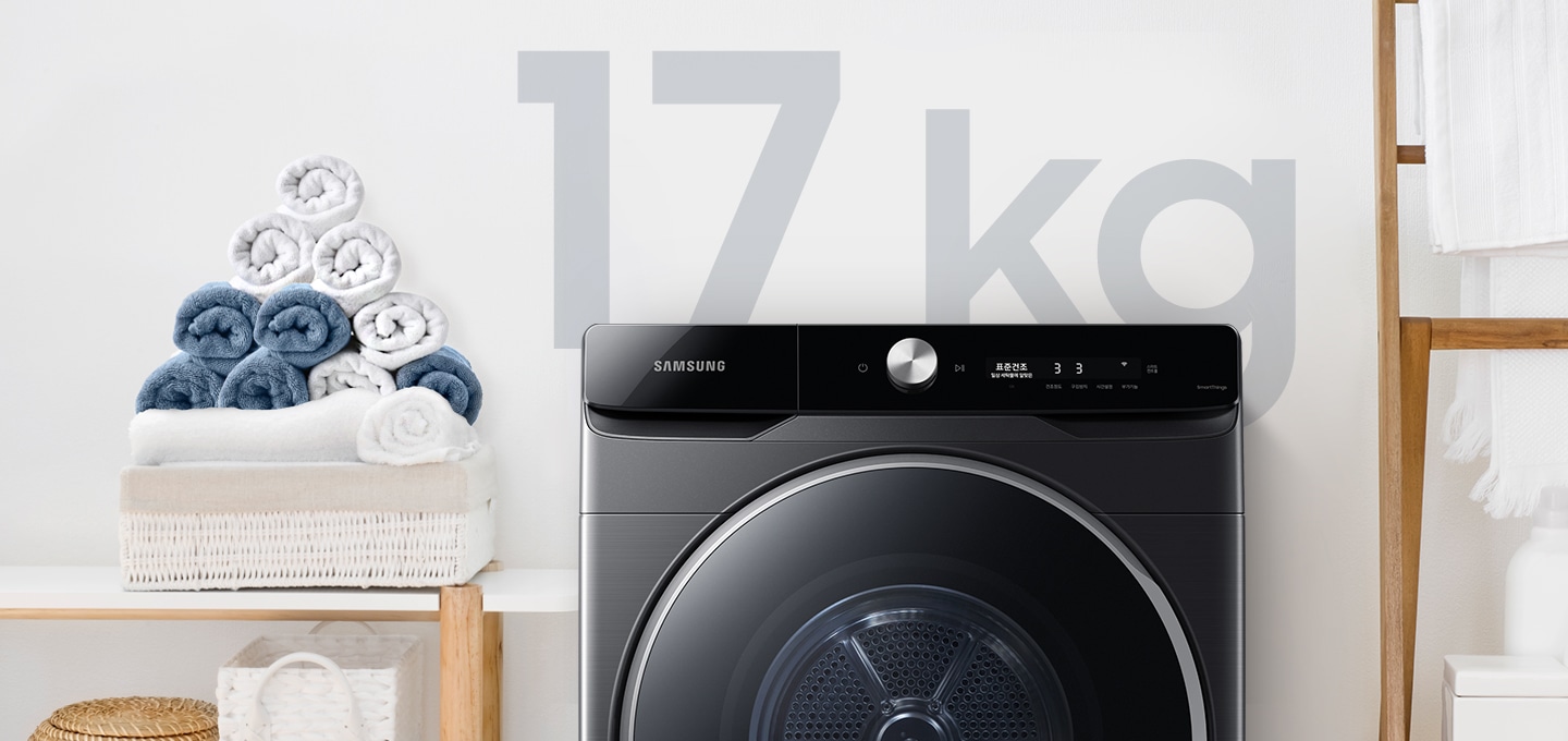 욕실로 보이는 공간에 삼성 그랑데 건조기 AI 제품이 놓여져 있습니다. 왼쪽 선반에는 수건이 쌓여져 있고 그 밑에는 바구니가 있습니다.