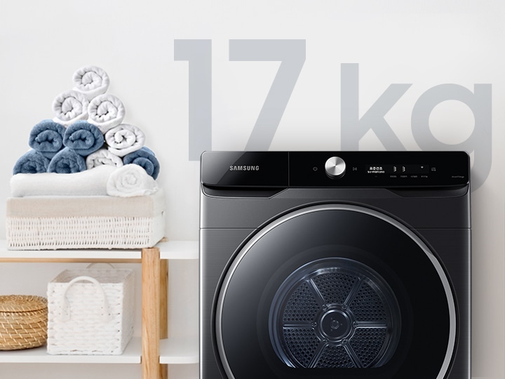 욕실로 보이는 공간에 삼성 그랑데 건조기 AI 제품이 놓여져 있습니다. 왼쪽 선반에는 수건이 쌓여져 있고 그 밑에는 바구니가 있습니다.