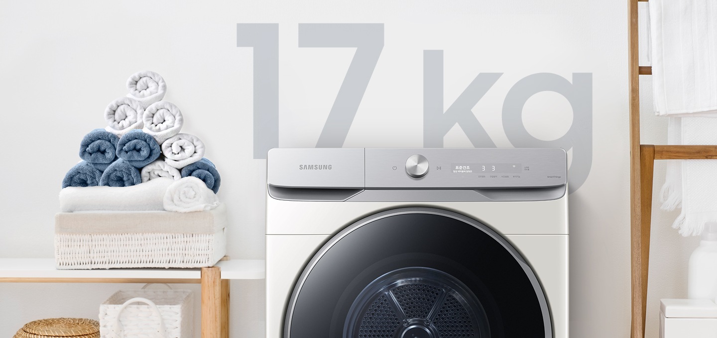 욕실로 보이는 공간에 삼성 그랑데 건조기 AI 제품이 놓여져 있습니다. 왼쪽 선반에는 수건이 쌓여져 있고 그 밑에는 바구니가 있습니다.