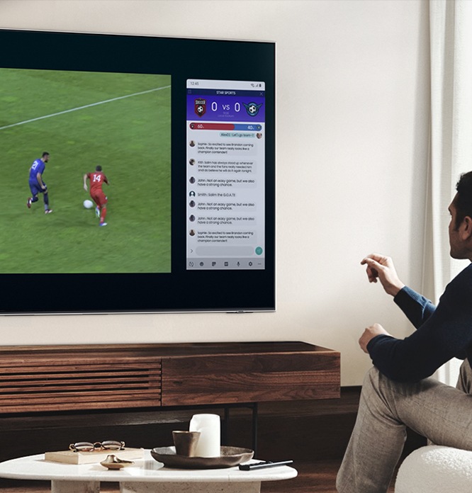 우측하단에는 구글 듀오 아이콘이 합성되어 있습니다. 우측 이미지는 벽걸이 TV 가 설치되어 있고 남성이 앉아 TV를 시청하고 있습니다. TV 온스크린에는 축구와 채팅화면이 두개로 나뉘어보입니다.