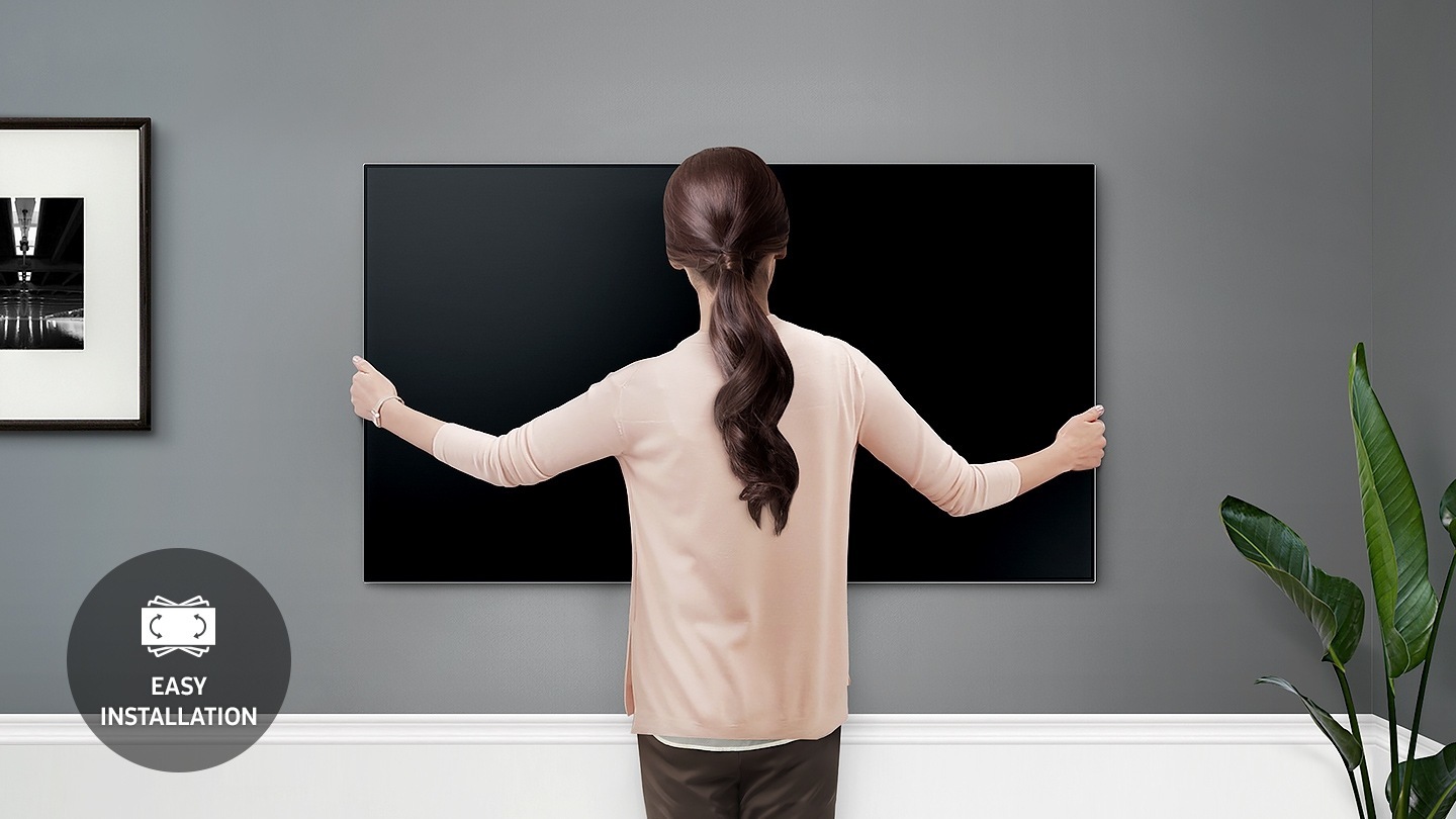 벽면에 TV를 설치하고 있는 여자의 뒷모습이 보입니다. 왼쪽 아래로 쉬운 설치 아이콘이 보입니다. 