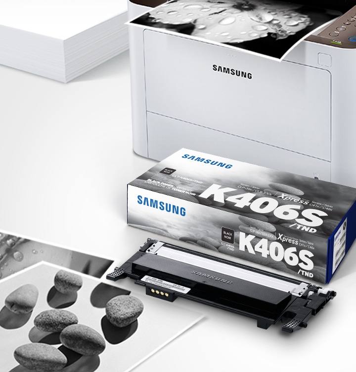 위쪽 삼성 프린터에서 출력물이 나오고 있고, 아래쪽 삼성 토너 카트리지가 있습니다.