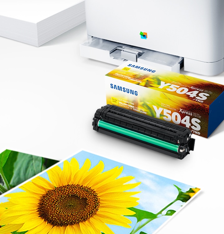 위쪽 삼성 프린터에서 출력물이 나오고 있고, 아래쪽 삼성 토너 카트리지가 있습니다.