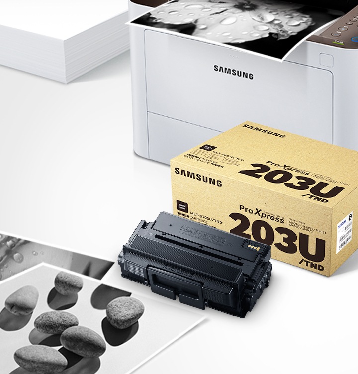 위쪽 삼성 프린터에서 출력물이 나오고 있고, 아래쪽 삼성 토너 카트리지가 있습니다.