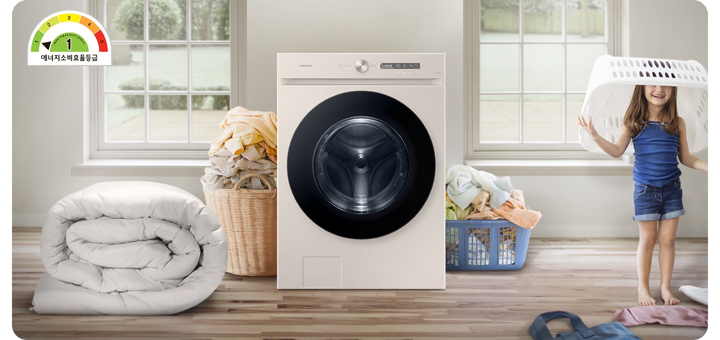 정면 가운데에 그랑데AI 세탁기 정면샷이 보입니다. 세탁기의 왼편에는 대형이불이있고 좌우로 많은 빨래가 보입니다. 화면 오른쪽 끝에는 바구리를 머리에 쓰고 웃고 있는 아이의 모습이 보입니다. 왼편 상단 위에는 에너지 소비효율 1등급 표시가 되어 있습니다.