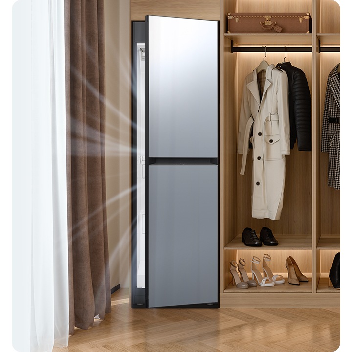 따뜻한 톤의 행거옷장이 좌측에 있고 옷걸이에는 옷이 두벌 걸려있습니다, 옷 위로는 캐리어 가방 있고, 아래에는 여러 개의 구두있습니다. 바로 옆 우측에는 에어드레서 드레스룸을 제습하고 있는 모습입니다.