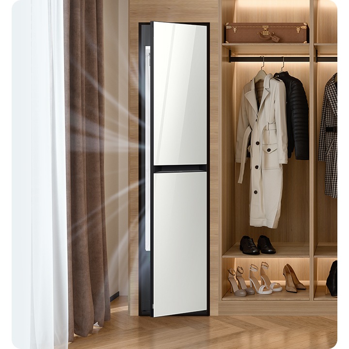 따뜻한 톤의 행거옷장이 좌측에 있고 옷걸이에는 옷이 두벌 걸려있습니다, 옷 위로는 캐리어 가방 있고, 아래에는 여러 개의 구두있습니다. 바로 옆 우측에는 에어드레서 드레스룸을 제습하고 있는 모습입니다.