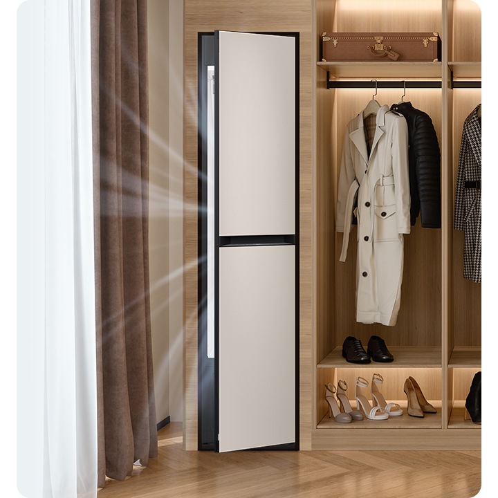 따뜻한 톤의 행거옷장이 좌측에 있고 옷걸이에는 옷이 두벌 걸려있습니다, 옷 위로는 캐리어 가방 있고, 아래에는 여러 개의 구두있습니다. 바로 옆 우측에는 에어드레서 드레스룸을 제습하고 있는 모습입니다.