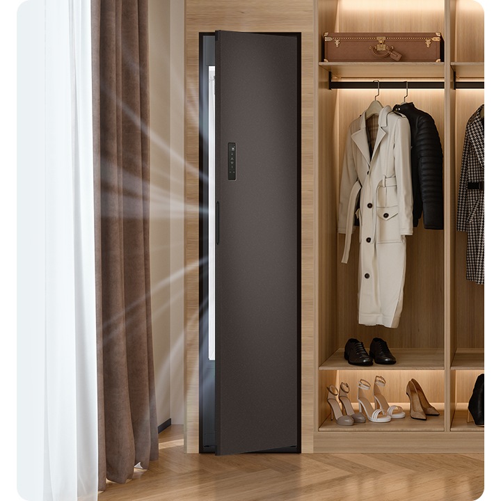 따뜻한 톤의 행거옷장이 좌측에 있고 옷걸이에는 옷이 두벌 걸려있습니다, 옷 위로는 캐리어 가방 있고, 아래에는 여러 개의 구두있습니다. 바로 옆 우측에는 에어드레서 드레스룸을 제습하고 있는 모습입니다.