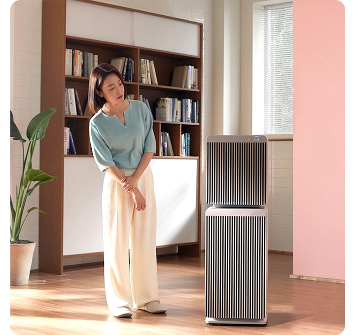 거실에서 한 사람이 공기청정기를 바라보고 있는 모습입니다.