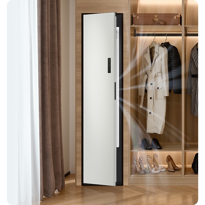 따뜻한 톤의 행거옷장이 좌측에 있고 옷걸이에는 옷이 두벌 걸려있습니다, 옷 위로는 캐리어 가방 있고, 아래에는 여러 개의 구두있습니다. 바로 옆 우측에는 에어드레서 드레스룸을 제습하고 있는 모습입니다.