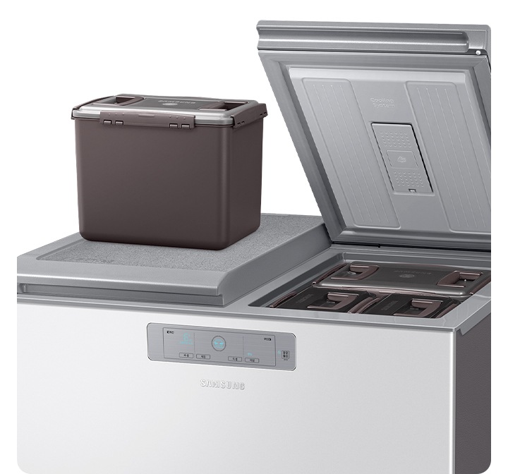 뚜껑형 김치냉장고가 열려있으며 한쪽에 김치통이 올려져 있습니다.