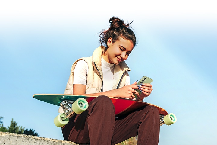 한 여성이 무릎에 스케이트보드를 얹은 채 밝은 햇살 아래 갤럭시 퀀텀4를 확인하고 있습니다.