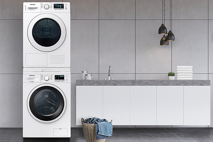 그레이 타일로 인테리어 되어있는 넓은 다용도실이 보이며, 좌측엔 비스포크 그랑데 AI 세탁기 건조기가 건조기 상단키트를 사용해 하나로 되어 있는 모습이 보이며, 가운데에 수납공간이 하단에 함께있는 세면대가 보이며 세면대 위 좌측엔 세탁세제 통이 보이고 우측엔 개어져 있는 하얀색 수건 6개가 보여지고 수건 우측엔 작은 흰 화분이 보여집니다.  세면대 앞엔 라탄의 빨래통과 안에 청바지 빨래가 들어있으며, 우측엔 사다리가 있으며 사딜에 상단에 수건이 걸려있고 두번째 칸에 수건이 개어져 있습니다.