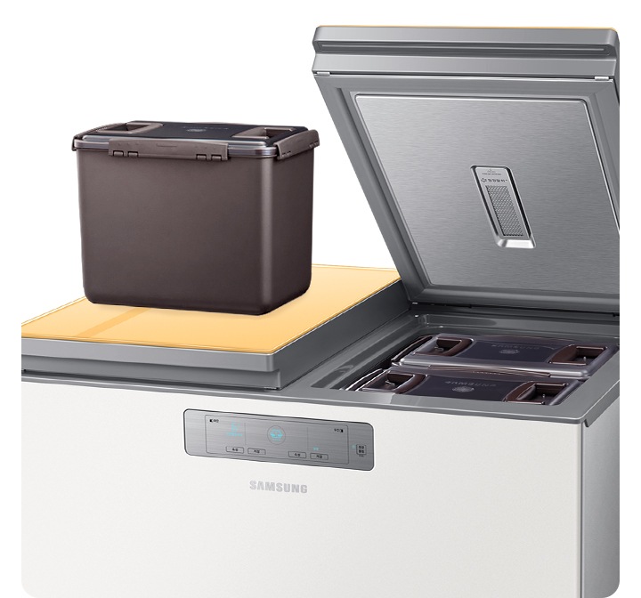 뚜껑형 김치냉장고가 열려있으며 한쪽에 김치통이 올려져 있습니다.