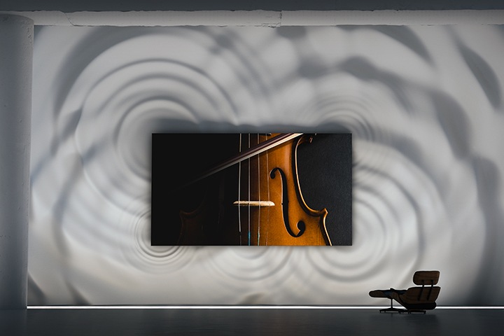 벽에 장착된 MICRO LED TV 화면 속에 클로즈업된 바이올린이 보입니다. TV 주변으로 거대한 파동 물결 그래픽이 묘사되어 있고, 이는 아레나 사운드를 형상화한 장면입니다.