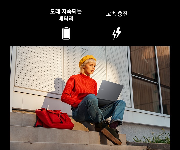 한 젊은 여성이 야외 건물 앞 계단에 앉아 갤럭시 북4 Pro를 사용하고 있습니다. 이미지의 상단에는 오래 지속되는 배터리와 고속 충전을 뜻하는 아이콘과 텍스트가 표시되어 있습니다.