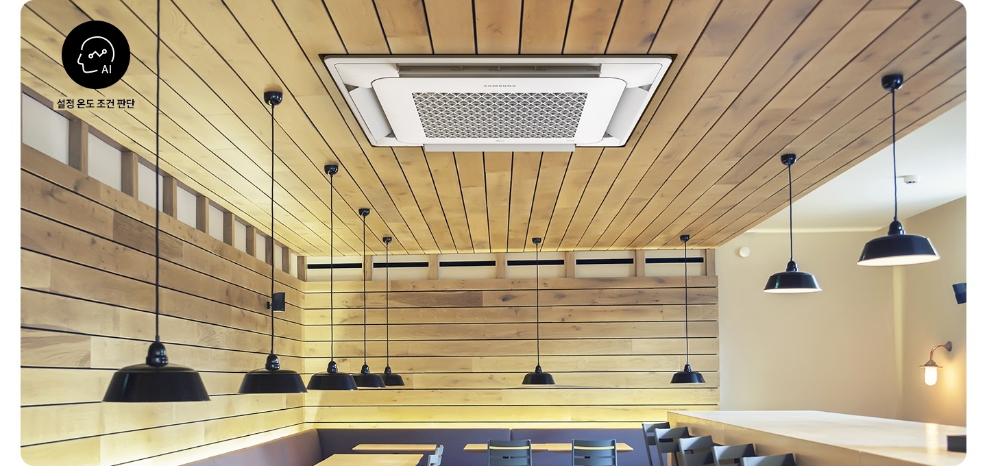 원목으로 인테리어 되어있는 카페공간에 내부의 천장 상단위주로 보여지며 각 자리마다 천장에 검은색 조명들이 철치 되어 있는 모습이 보여지며 좌측 상단에 사람 머리 모양의 ai문구와 설정 온도 조건 판단 문구와 함께 아이콘이 보여지며 가운데 천장 에는 4way 시스템에어컨이 작동하고 있는 모습이 보여집니다. 