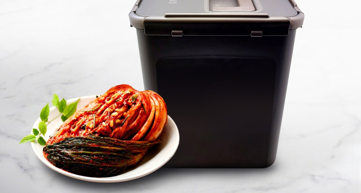 김치통 모서리 부분을 클로즈업하여 보여주고 있으며 좌측에는 접시위에 김치가 놓여져 있습니다.