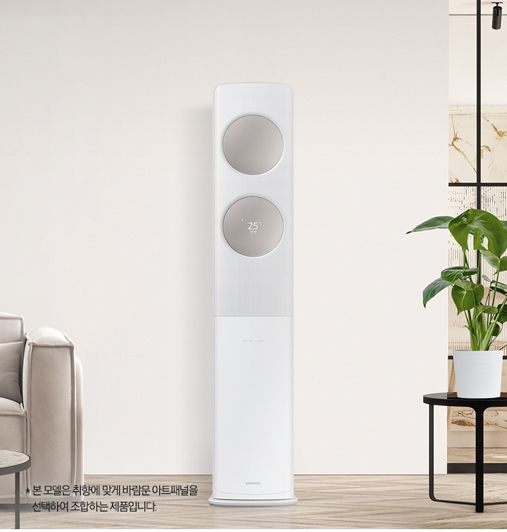 베이지 톤으로 인테리어 되어있는 공간에 좌측엔 2인용 쇼파가 보여지고 쇼파 앞에는 원형 탁자와 탁자위에 책과 화병들이 보여집니다. 가운데에는 무풍 클래식 에어컨이 위치해 있으며, 바람문은 메탈릭 베이지 바람문이 장착되어 있습니다. 우측엔 다이닝 룸으로 가는 중문이 있고 그 앞에 일인용 쇼파와 작은 탁자위 화분이 함께 보여집니다