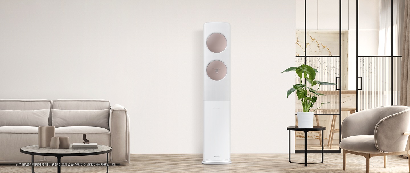 베이지 톤으로 인테리어 되어있는 공간에 좌측엔 2인용 쇼파가 보여지고 쇼파 앞에는 원형 탁자와 탁자위에 책과 화병들이 보여집니다. 가운데에는 무풍 클래식 에어컨이 위치해 있으며, 바람문은 메탈릭 로즈골드 바람문이 장착되어 있습니다. 우측엔 다이닝 룸으로 가는 중문이 있고 그 앞에 일인용 쇼파와 작은 탁자위 화분이 함께 보여집니다