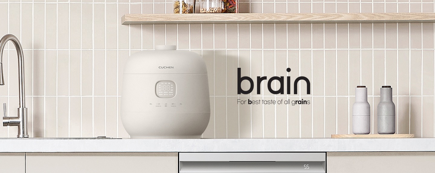 연한 파란색 벽과 브라운톤 바닥 배경에 왼쪽에 책 3권이 있습니다. 책 바로 옆에는 쿠첸 밥솥 정명이 있습니다. 오른쪽에는 타이틀 brain, for best taste of all grains 문구가 있습니다.