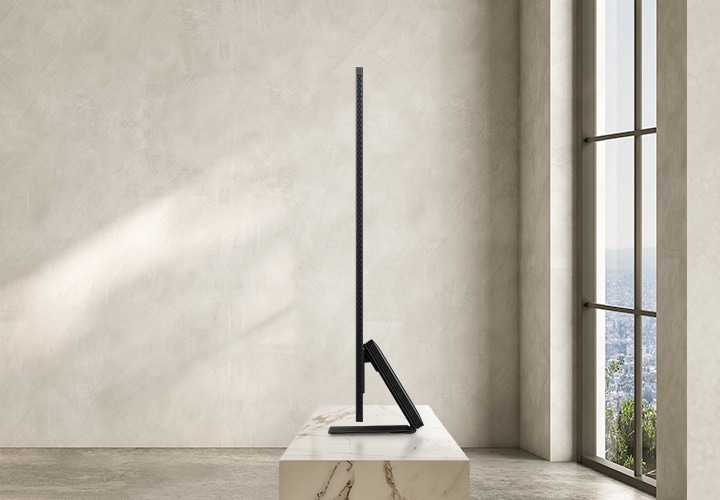 TV 우측 측면이 보입니다. TV 아래에는 장식장이 있으며 뒤로는 큰 창이 있습니다.