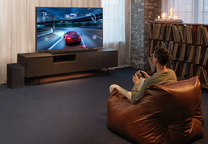 남성이 소파에 앉아 게임을 하고 있습니다. TV에는 레이싱 게임화면이 보이고 있습니다. 