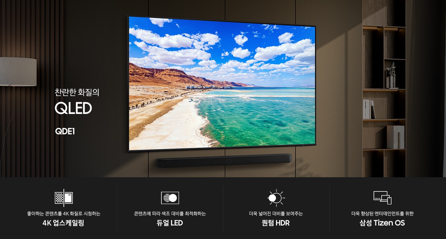 벽면에 TV와 사운드바가 설치되어 있습니다. TV 화면에는 해변이 보입니다. TV 오른쪽에는 장식장이 있으며, 장식장에는 책과 장식품이 놓여 있습니다. 찬란한 화질의 QLED QDE1 KV입니다. KV 하단에는 좋아하는 콘텐츠를 4K 화질로 신청하는 4K 업스케일링, 콘텐츠에 따라 색조 대비를 최적화하는 듀얼 LED, 더욱 넓어진 대비를 보여주는 퀀텀 HDR, 더욱 향상된 엔터테인먼트를 위한 삼성 Tizen OS 문구와 아이콘이 있습니다.