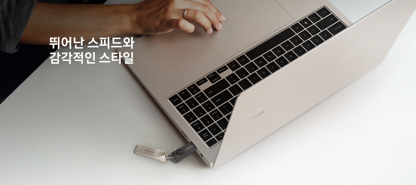 화이트 색상의 책상 위에 제품을 연결한 노트북을 올려두고 한 손으로 작업을 하고 있는 모습을 위에서 내려본 이미지입니다. 이미지 왼쪽 상단부분에는 약간 어두운 부분이 있고 그 위에 뛰어난 스피드와 감각적인 스타일 텍스트가 적혀 있습니다.