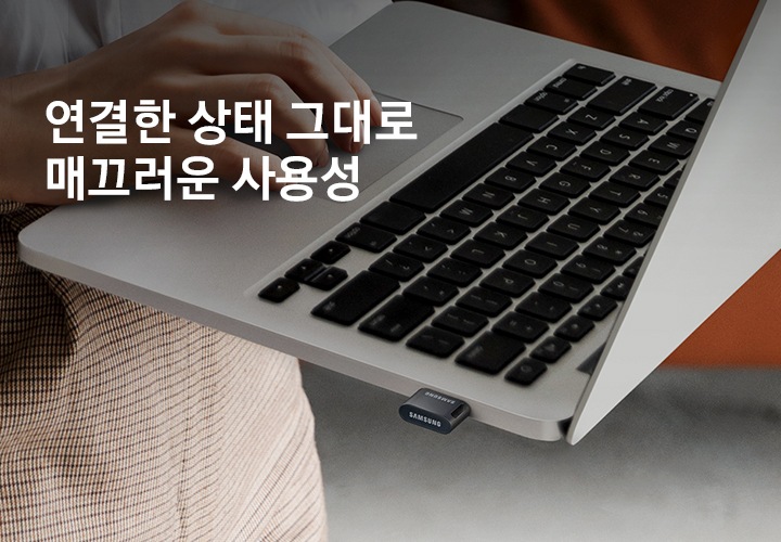 한 사람이 USB 3.1 FIT PLUS 512 GB 제품이 연결된 노트북을&nbsp;한 손으로&nbsp;들고&nbsp;다른 손으로&nbsp;작업을 하고 있는 모습을 보여주고 있습니다. 이미지 왼쪽&nbsp;상단부분에는&nbsp;약간 어두운 부분이 있고 그 위에 연결한 상태 그대로 매끄러운 사용성 텍스트가 적혀 있습니다.