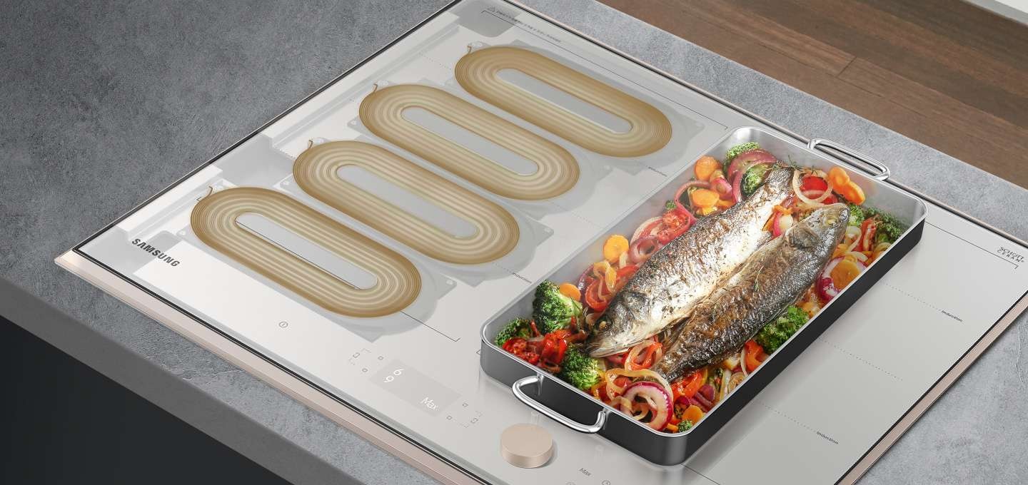 짙은 그레이색 상판에 BESPOKE 인덕션 빌트인 Infinite Line 그레이지가 설치되어 있으며, 인덕션의 좌측에는 내부 4개의 코일을 보여주고 있고, 우측에는 직사각 스텐팬 안에 채소와 생선이 요리되고 있습니다.