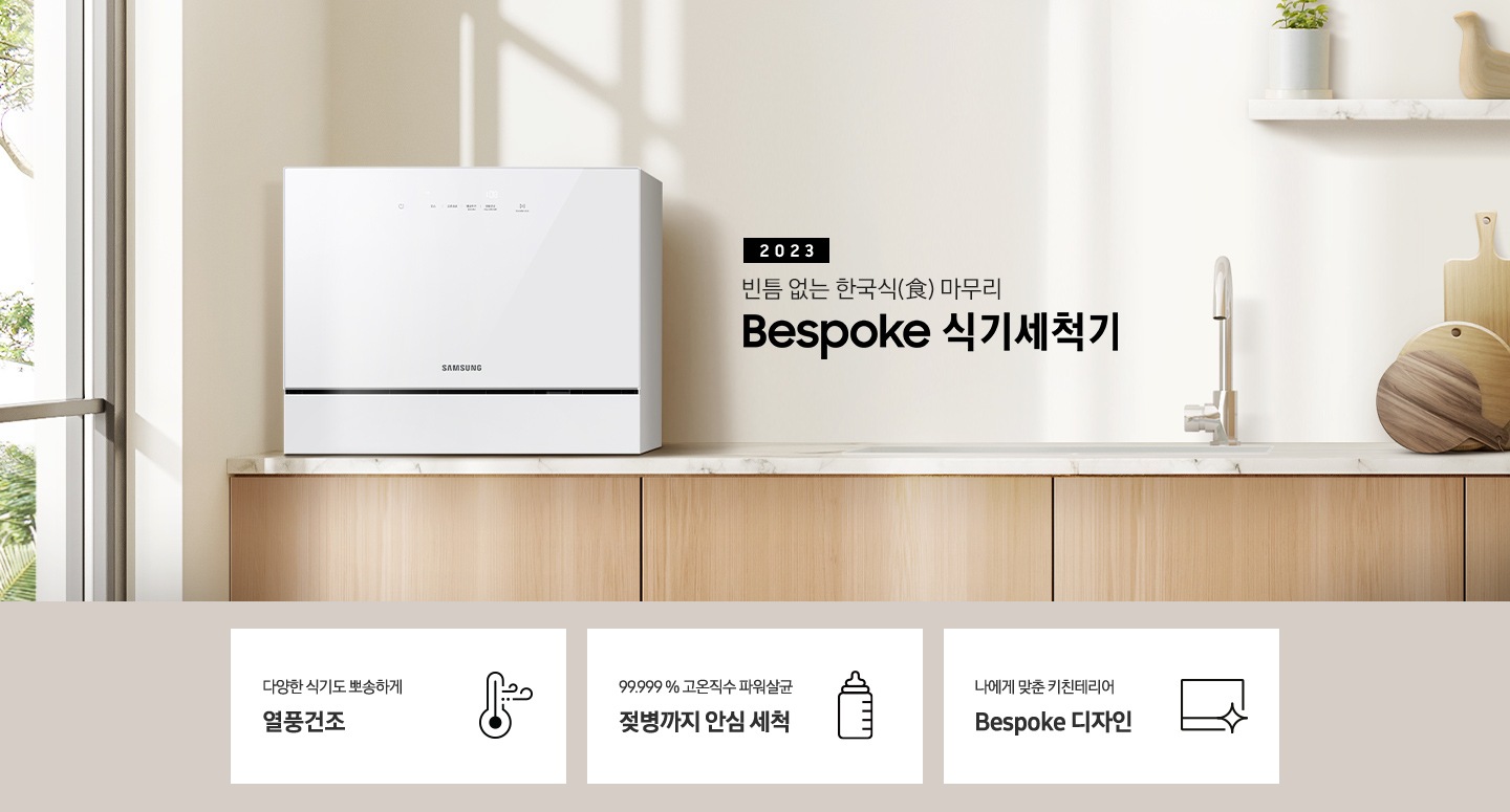 우드 패널 주방 왼쪽엔 창문이 보이고 상판 위 카운터탑 이 올려져 있습니다. 우측에는 2023 빈틈 없는 한국식 마무리 BESPOKE 식기세척기 라는 슬로건이 적여 있고 싱크대 오른쪽엔 수전과, 나무 도마 3개가 있습니다. 그 위 선반에는 작은 식물이 있는 화분과 새 모양의 오브제가 올려져 있습니다.