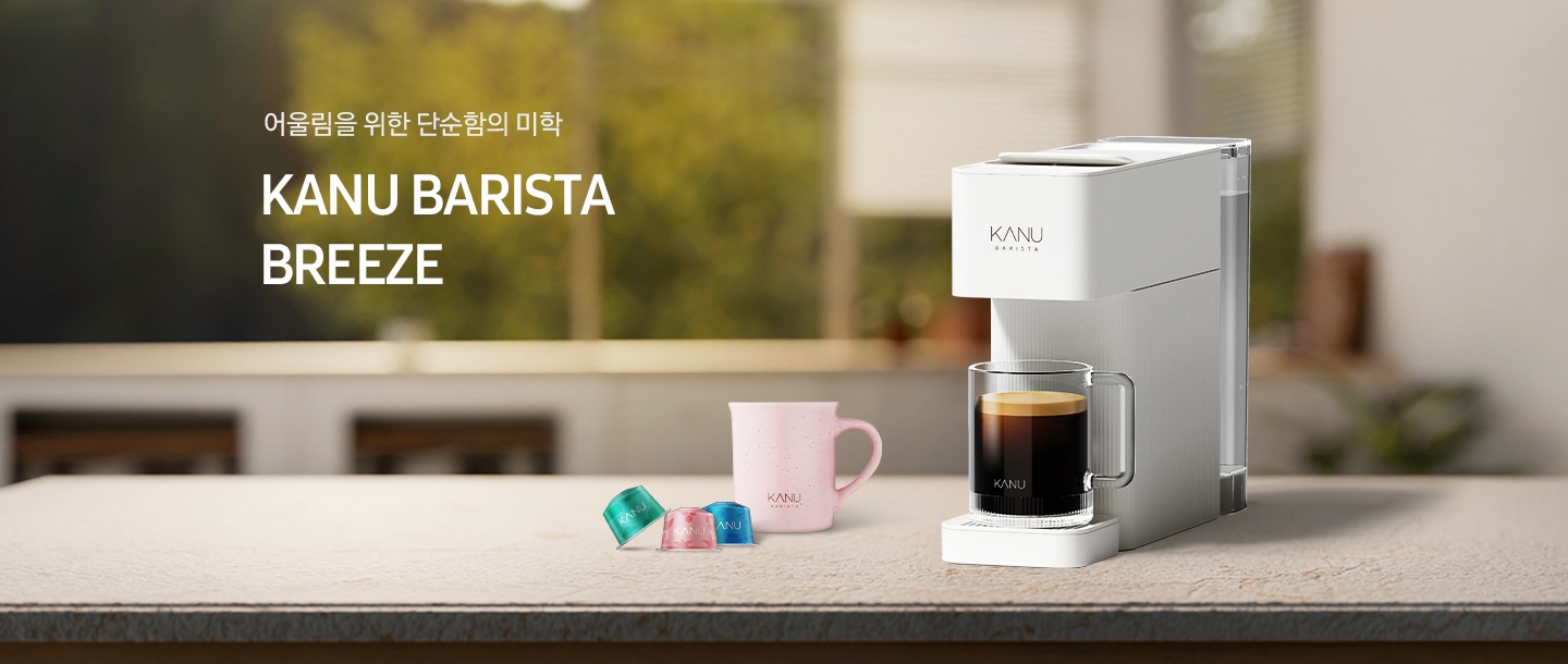 아일랜드 식탁 위 우측에 카누 바리스타 브리즈 크림 화이트 캡슐 커피머신이 놓여있고 머신 위에 머그잔에는 아메리카노가 담겨있습니다. 머신 좌측에는 분홍색 카누 머그잔과 카누 캡슐커피머신 전용 캡슐 3개가 놓여있습니다. 좌측에는 문구가 나와있습니다. 어울림을 위한 단순함의 미학. KANU BARISTA BREEZE