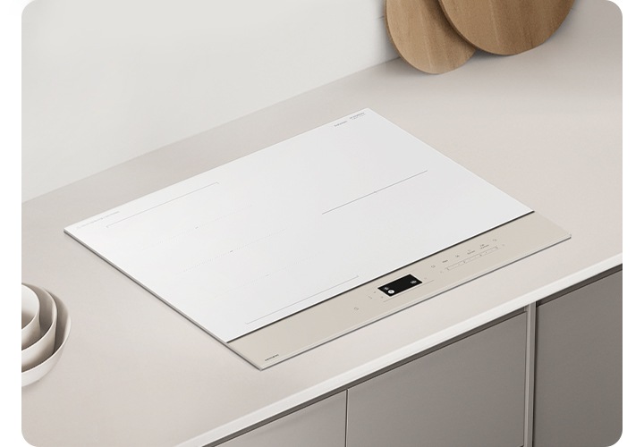 그레이톤 우드 패널에 그레이 톤 대리석 상판이 깔린 주방 테이블이 보입니다. 테이블 가운데에는 BESPOKE 전기 레인지가 설치되어 있습니다. 전기레인지 왼쪽에는 회색 화병과 검은색 세제 통이 보이고 오른쪽 상단으로는 흰색 원통 모양의 도자기 수저 통 안에 원목 수저가 꽂혀 있습니다.