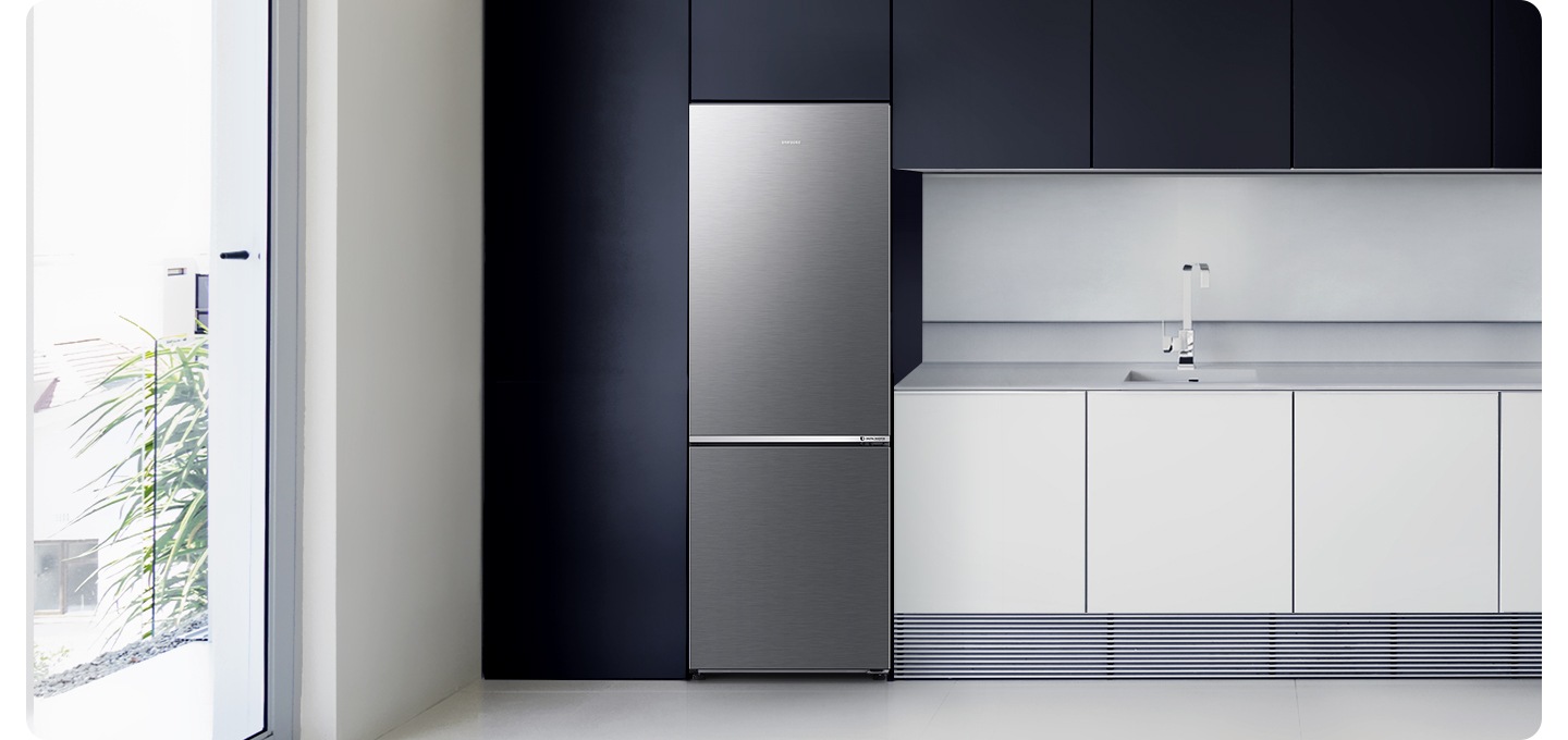 화이트&네이비톤 주방 인테리어컷 입니다. 좌측에 하얀색 몰딩의 통창 밖으로 주택과 나무가 보입니다. 네이비색 냉장고장에 리파인드 이녹스 컬러 냉장고가 설치되어 있습니다. 냉장고 우측으로는 크림색 패널의 하부장과 수전이 나와있습니다.