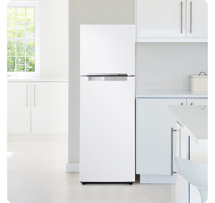 화이트톤 주방 인테리어컷 입니다. 좌측으로는 오픈된 공간에 작은 창문과 하얀색 수납장이 있습니다. 우측은 싱크대와 아일랜드 식탁이 있는 인테리어컷으로 리파인드 이녹스 컬러의 일반 냉장고가 중앙에 놓여있습니다.