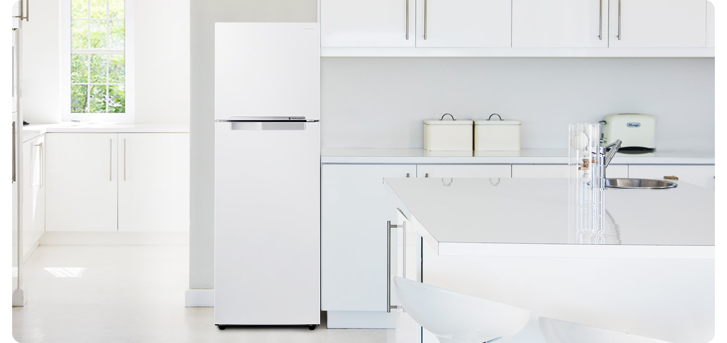 화이트톤 주방 인테리어컷 입니다. 좌측으로는 오픈된 공간에 작은 창문과 하얀색 수납장이 있습니다. 우측은 싱크대와 아일랜드 식탁이 있는 인테리어컷으로 리파인드 이녹스 컬러의 일반 냉장고가 중앙에 놓여있습니다.