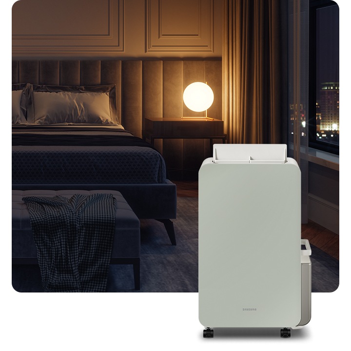 불이 꺼진 침실 안 침대 옆 원형 조명 하나가 켜져있고  앞에 삼성 인버터 제습기가 서 있습니다.