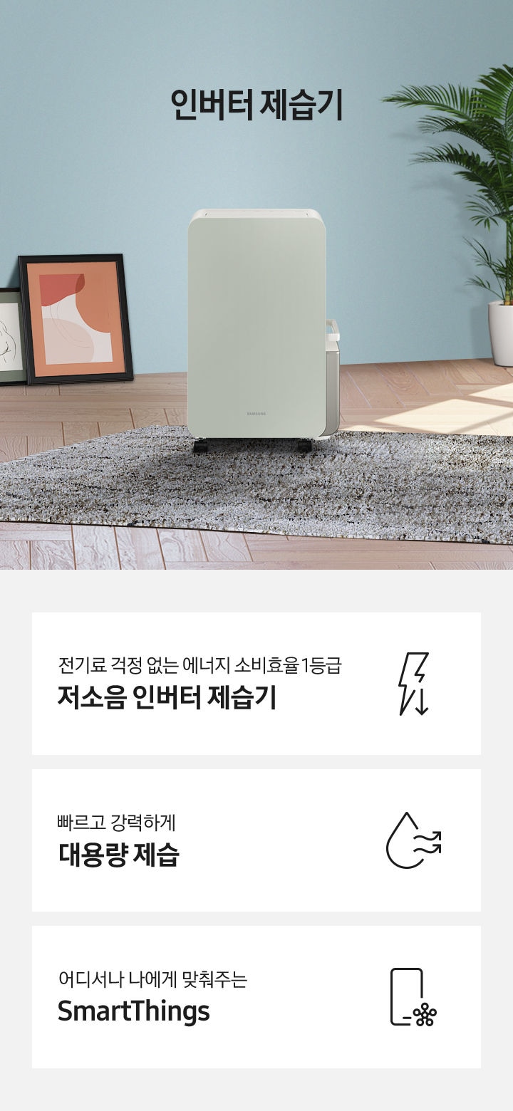 마루 위 회색 러그가 깔려 있고 삼성 인버터 제습기가 있습니다. 제습기 왼쪽에는 액자 두 개가 보이고 오른쪽으로는 야자 나무와 회색 의자가 하나 놓여 있습니다.