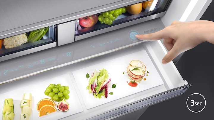 냉장고 내상 셰프 팬트리 부분이 오픈되어 있고 안에 각종 과일과 채소가 가지런히 놓여있는 모습입니다. 팬트리 상단에 디스플레이 화면이 나와있으며 우측에 컨트롤 버튼을 누르는 손 사진이 나와있습니다.