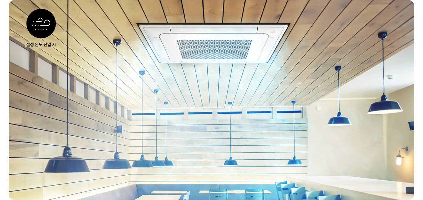우드로 인테리어 되어있는 스터디 카페로 처럼 보여지는 공간에 천장 방향으로 바닥이 보이지 않게 보여지고 좌측 상단에 바람모양의 아이콘과 설정 온도 진입시 문구가 보여지고 가운데 천장에 4Way 천장형 시스템에어컨 이 설치되어 무풍으로 작동되는 모습이 보여집니다.